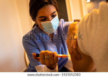 Young nurse with mask giving insulin shot to patient at home visit.