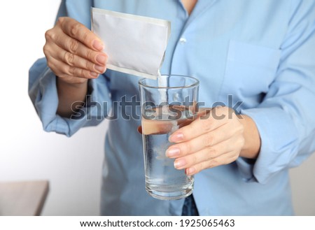 Woman pouring powder from medicine sachet into glass with water, closeup