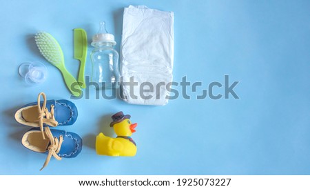 Baby care accessories, newborn baby diaper, pacifier, comb and hair brush, bottle, little boy shoes and toy on a blue background. Wish list or shopping overview for pregnancy, baby shower concept. Royalty-Free Stock Photo #1925073227