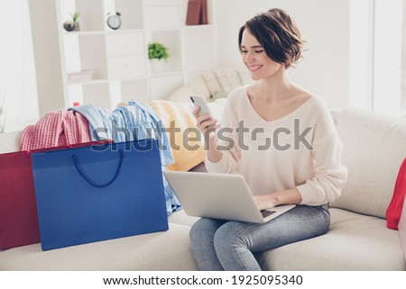 Photo of happy brunette woman sit sofa look phone hold laptop shop online bags indoors relax home living-room