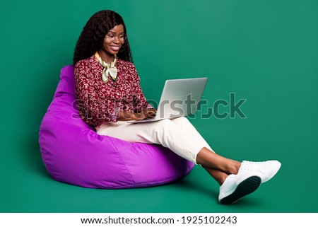 Photo of cute pretty curly dark skin woman dressed red shirt sitting bean bag typing modern device isolated green color background