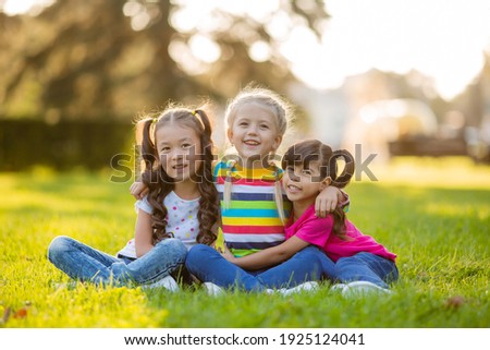 three little girls cuddle in the summer on the lawn. International Children's Day Royalty-Free Stock Photo #1925124041