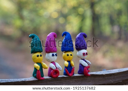 Four plasticine dwarfs stand in the forest on a colored background. Next to them is the inscription love.