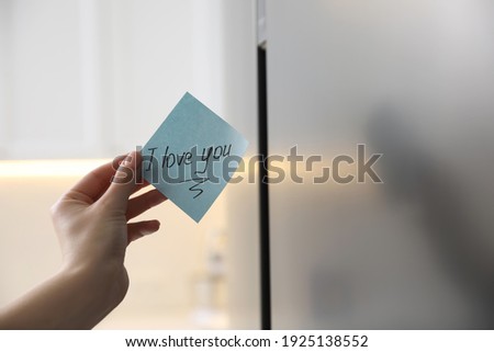 Woman with sticky note saying I Love You near fridge door, closeup. Romantic message