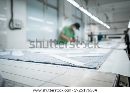 Man wearing medical mask with cutter machine and personal protective equipment at garment industrial work place. Fabric cutter in AsianTextile cloth factory working process tailoring workers equipment Royalty-Free Stock Photo #1925196584