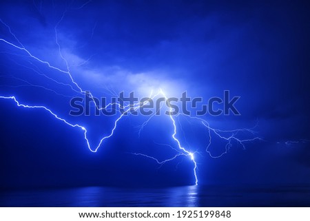 A huge branched lightning strikes the sea near a distant ship with a reflection Royalty-Free Stock Photo #1925199848