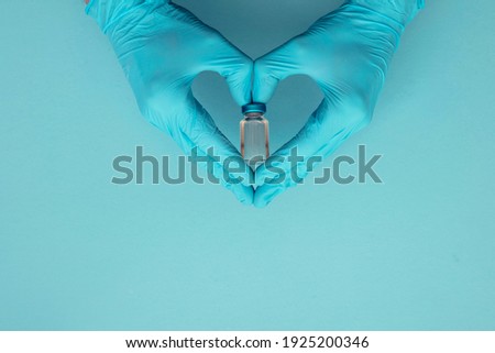Doctor or nurse wearing blue gloves holding vaccine dose in a heart shape