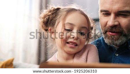 Close up of joyful caring Caucasian bearded dad with small daughter in room together videochatting using tablet. Father teaching small girl to use gadget device, family time, watching cartoons at home