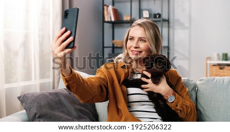 Close up portrait of positive beautiful Caucasian woman smiling posing to smartphone camera taking selfie photos with animal dog, joyful female with puppy pet taking pictures on cellphone at home