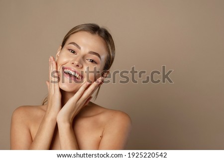 A happy laughing young woman with perfect skin, natural make-up and a beautiful smile. Female portrait with bare shoulders on a beige background