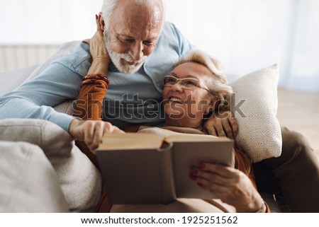 Mature smiling couple having fun on the sofa while reading a book Royalty-Free Stock Photo #1925251562