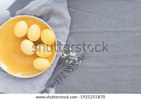 Dish with colored yellow eggs on easter, gray cloth background, gypsophila flowers flat lay