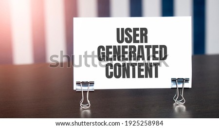USER GENERATED CONTENT sign on paper on dark desk in sunlight. Blue and white background