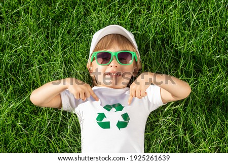 Happy child points fingers at recycle sign on t-shirt. Funny kid against spring green background. Ecology and Earth day concept. Top view