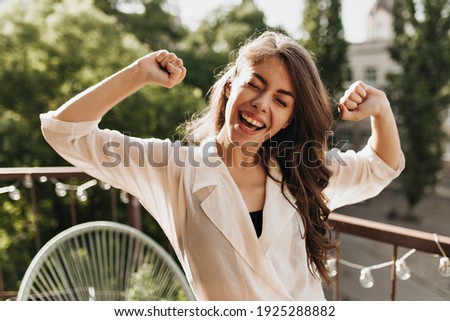 Lady in shirt having fun on balcony. Portrait of happy young woman in beige blouse sincerely smiling and posing on terrace