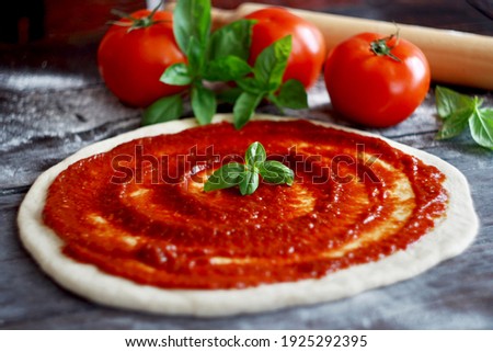 Raw pizza dough with tomato sauce and basil leaves. Selective focus