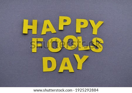 Inscription of the day fools of yellow letters carved from paper and laid out on a gray background in the style of minimalism. High quality photo