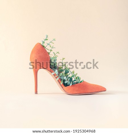 Minimal sustainable fashion concept with orange high heels and green leaves on beige background. Environmental protection and sustainability idea. Eco friendly aesthetics. Royalty-Free Stock Photo #1925304968