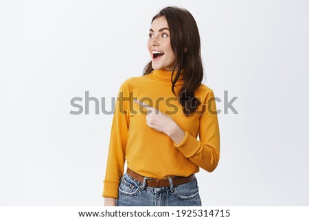 Excited beautiful girl checking out special deal in store, pointing and looking down with opened mouth and fascinated face, seeing good offer, white background. Royalty-Free Stock Photo #1925314715