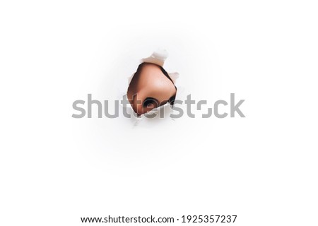 The male big nose protrudes through a torn hole in white paper. The concept of curiosity, espionage, sniffing, parfume. Background, copy space. Royalty-Free Stock Photo #1925357237