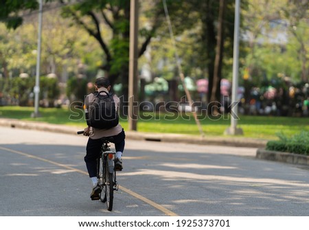 The back view of a man carries a black backpack and riding a bicycle in the park.
