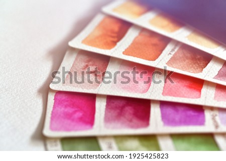 Close-up color palette in shades of pink, brown and orange. Lies on a white background, for the selection of colors, watercolor paper with filled rectangles, beautiful stains of paint.