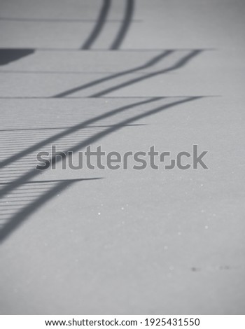 abstract of black shadows of fence in fresh white snow lines looking like ladders for background or graphic design 