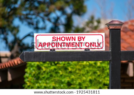 Shown By Appointment Only real estate sign on wooden post. Blurred green landscaping and clay tile roof background
