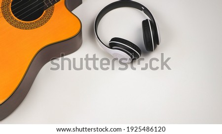 Top view or flat lay of acoustic guitar and  white headphones on white  background with copy space. Musician and hobby concept.