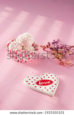 white concfets sprinkled with coconut shavings lie on a pink background. candy in the shape of hearts