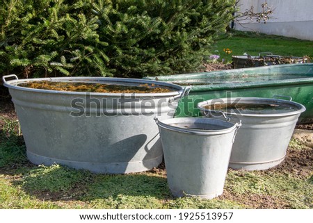 Three old zinc tubs and buckets in a garden. They are filled with water and are used as small garden ponds. Royalty-Free Stock Photo #1925513957