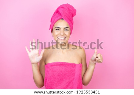 Young beautiful woman wearing shower towel after bath standing over isolated pink background showing and pointing up with fingers number six while smiling confident and happy