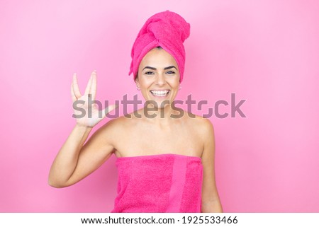 Young beautiful woman wearing shower towel after bath standing over isolated pink background doing hand symbol