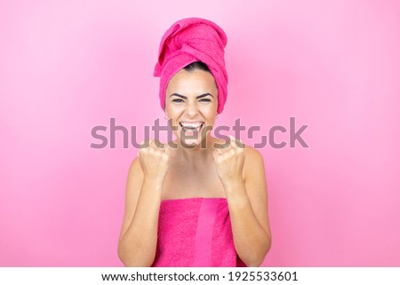 Young beautiful woman wearing shower towel after bath standing over isolated pink background very happy and excited making winner gesture with raised arms, smiling and screaming for success.