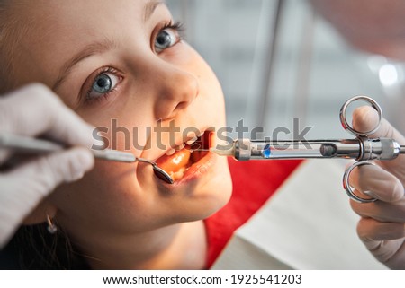 Little girl at dentist office, getting local anesthesia injection into gums. Cropped view of the dentist numbing gums for dental work. Pediatric dental care concept