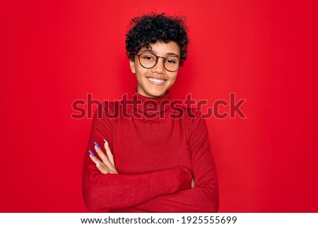 Young beautiful african american afro woman wearing turtleneck sweater and glasses happy face smiling with crossed arms looking at the camera. Positive person.