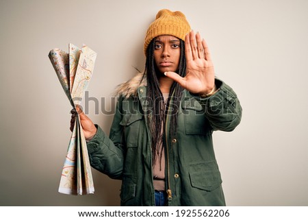 Young african american girl going on vacation holding turist city map over isolated background with open hand doing stop sign with serious and confident expression, defense gesture