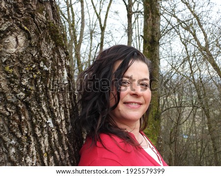 happy woman with long hair stands in front of a large tree