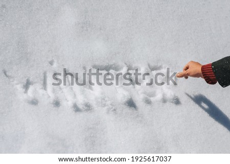 A man in a coat writes with his hand, draws letters and the word winter on the white fresh snow. Photography, concept, top view.