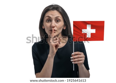 Happy young white woman holding flag of Switzerland and holds a finger to her lips isolated on a white background.