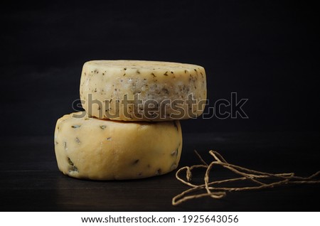 Two Caciotta cheese heads with spices and rope on a dark background. Side view. Traditional Italian delicacy.