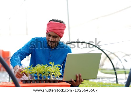 Young indian farmer using laptop at greenhouse or poly house