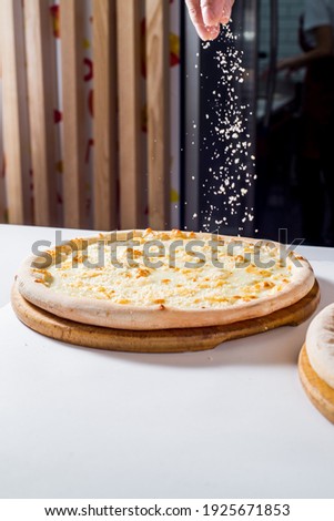 Cook sprinkles the cheese on the pizza. Cooking pizza