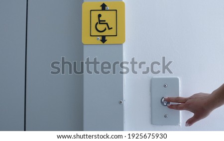 female hand presses the button to call the elevator inside, yellow sign of the possibility of using the elevator for people with disabilities, calling the elevator in a residential building