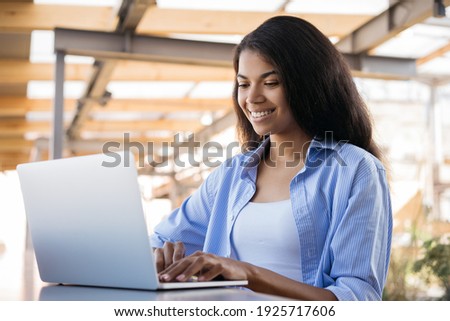 Young smiling African American woman using laptop computer working online sitting in cafe. Female copywriter typing, working freelance project at workplace 