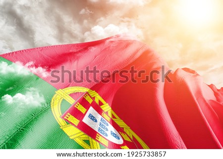 Portugal national flag cloth fabric waving on beautiful grey sky.