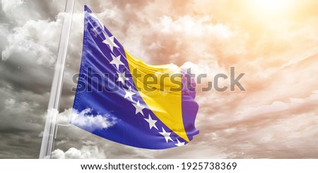 Bosnia and Herzegovina national flag cloth fabric waving on beautiful grey sky.