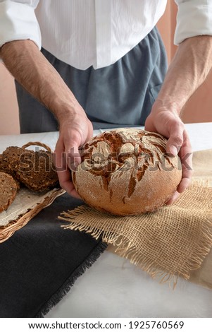 A hearth bread is a baked product without filling, made by baking a dough (consisting of at least flour and water), loosened with yeast or sourdough. Bread in the hands of a man. Royalty-Free Stock Photo #1925760569