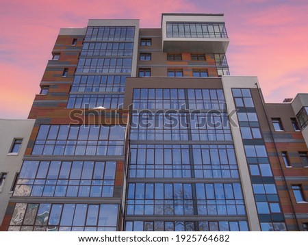 Modern exterior of the building. Glazed facade of the business office. The complex geometric and color, wooden shapes of the hotel skyscraper. City house on the background of the sunset pink sky.