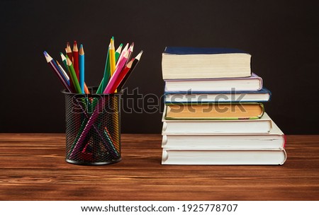 Colored pencils, a stack of books on a wooden table on a black background.